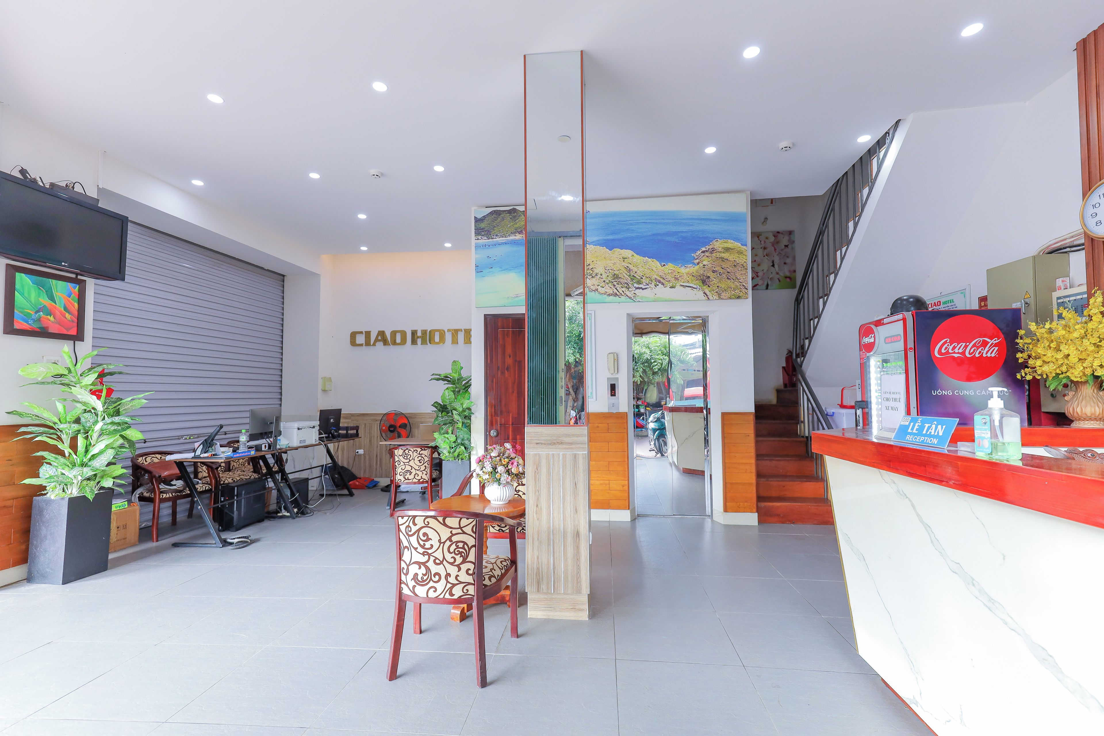 A hotel reception area with a desk, chairs, a staircase, and a wall with a painting.