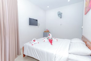 Een slaapkamer met een bed, een nachtkastje, een aan de muur bevestigde telefoon en een ventilator.