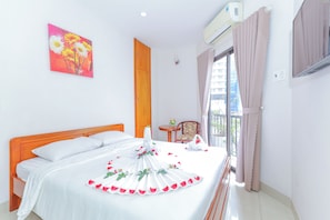 Een hotelkamer met een bed, een houten kledingkast, een tafeltje met een vaas en een raam met gordijnen.