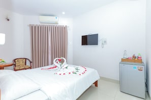 Een hotelkamer met een bed, een bureau, een stoel, een televisietoestel en een koelkast.