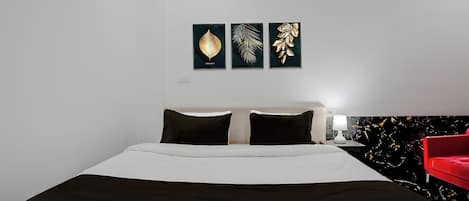 A hotel room with a bed, a red chair, and wall art.