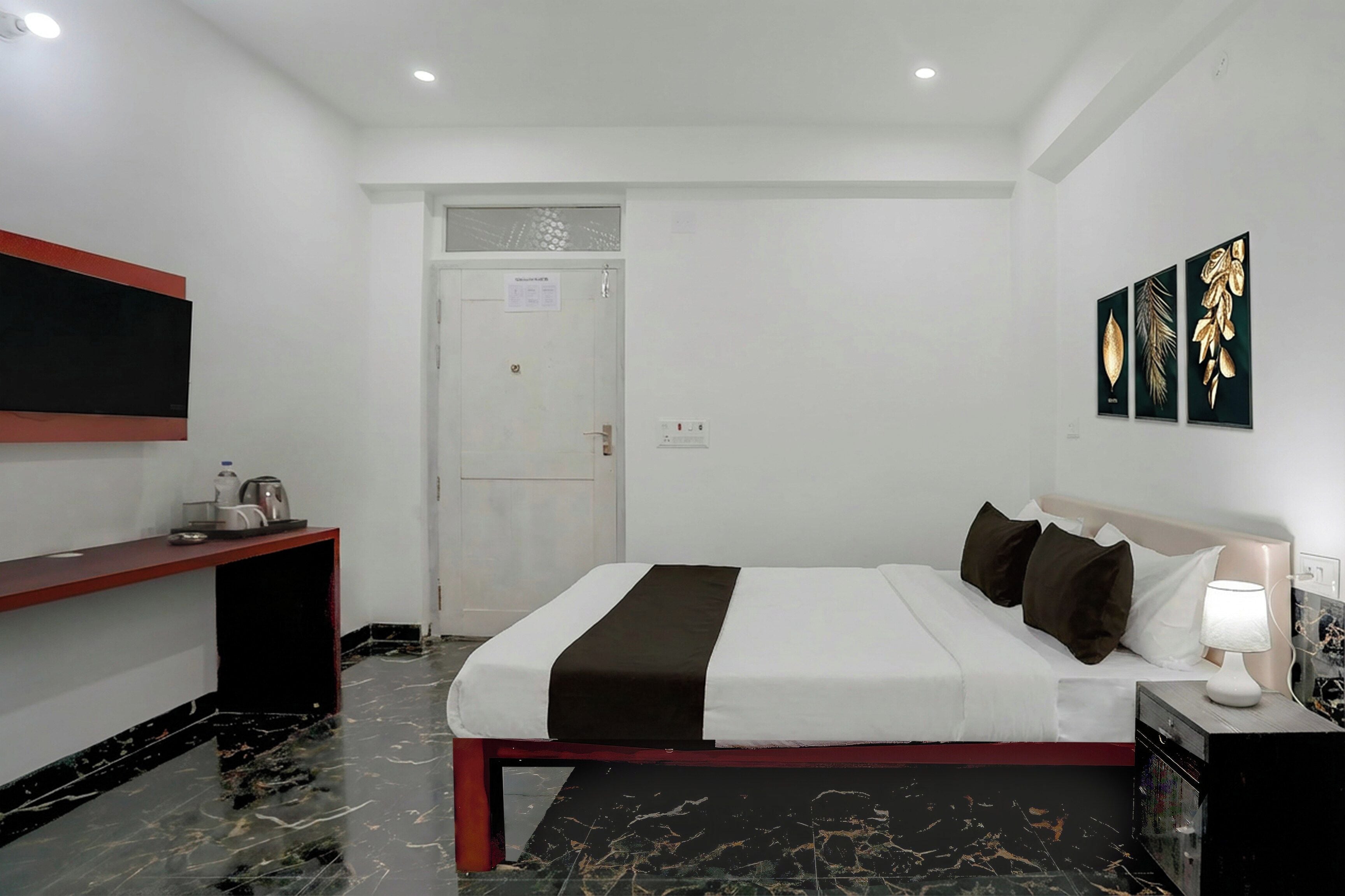 Una habitación de hotel con cama, mesita de noche, lámpara, obra de arte y una puerta.