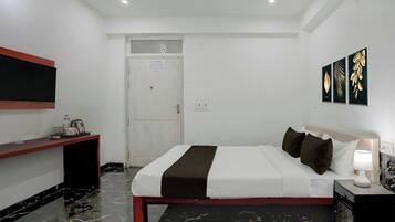 Una habitación de hotel con cama, mesita de noche, lámpara, obra de arte y una puerta.