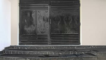 Una reja de metal negro con diseños decorativos, ubicada frente a una pared blanca, con escalones que conducen hacia ella.