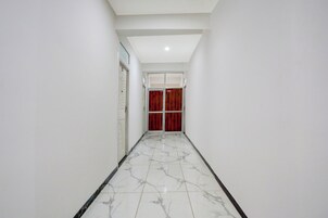 Un pasillo con paredes blancas, piso de mármol y una puerta roja al final.