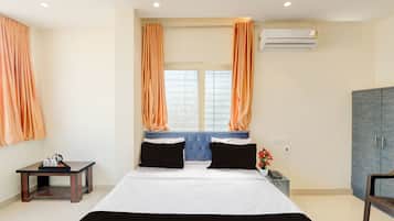 Una habitación de hotel con una cama, una mesita con hervidor, una silla, un equipo de aire acondicionado y un armario.
