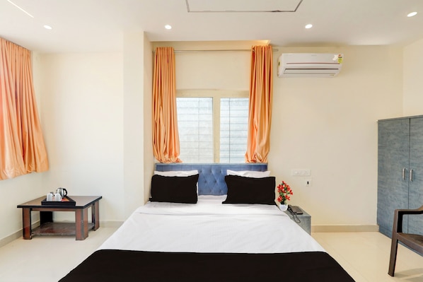 A hotel room with a bed, a small table with a kettle, a chair, an air conditioning unit, and a wardrobe.