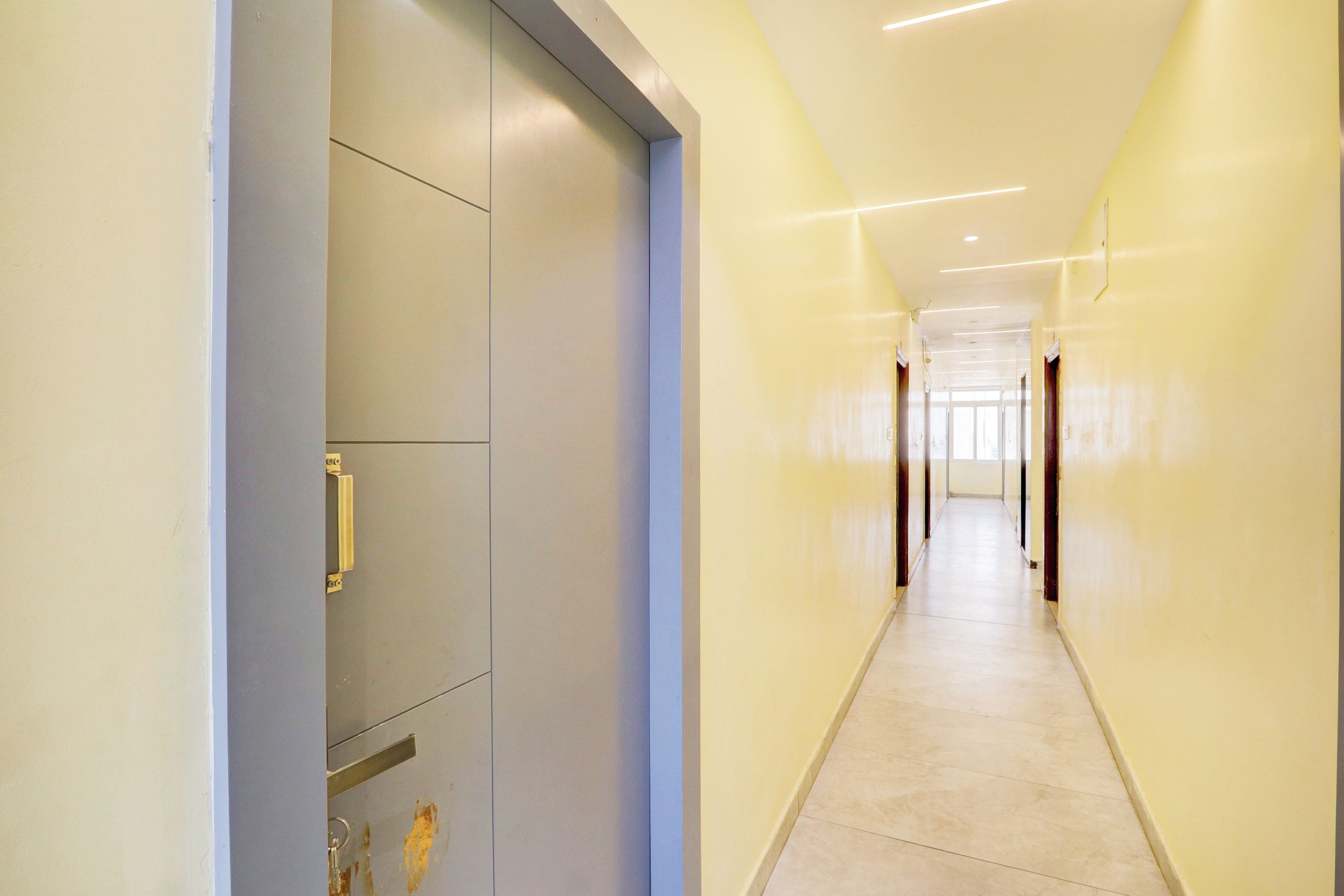 A long, narrow hallway with a door on the left and a series of doors on the right, leading to a bright room at the end.