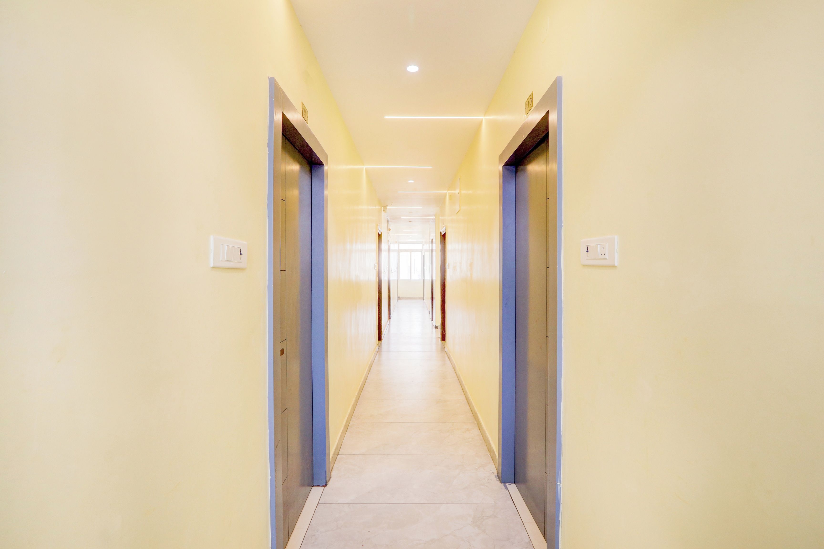 Un pasillo largo y estrecho con puertas a ambos lados, que conduce a una habitación luminosa al final.