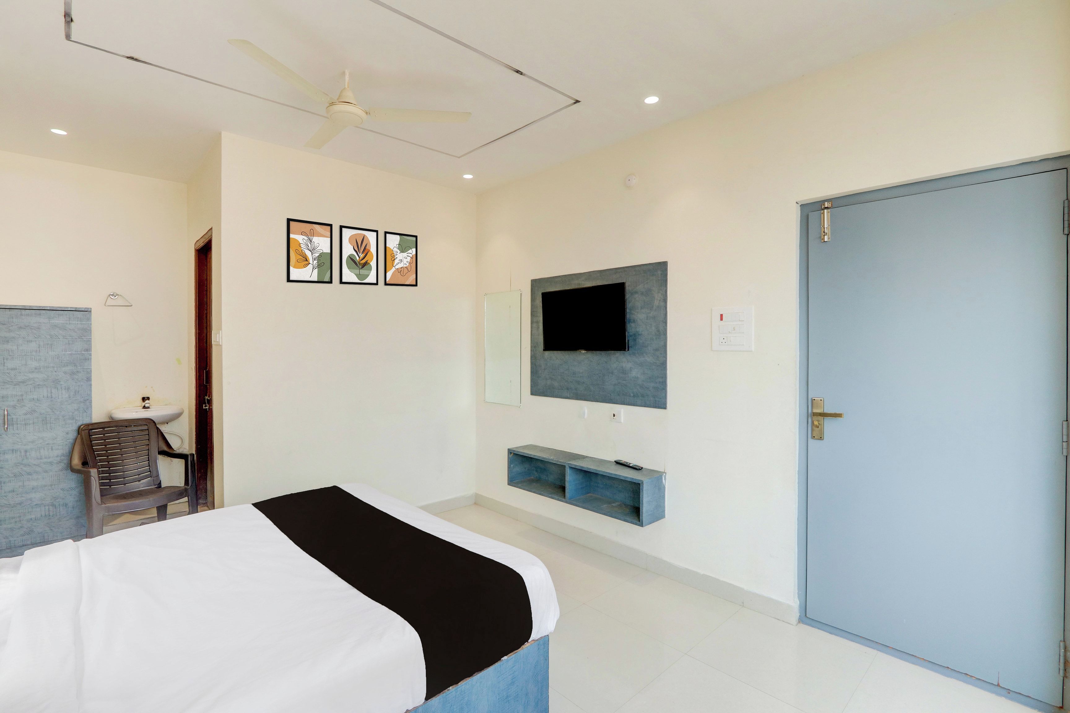 A bedroom with a bed, a ceiling fan, a TV mounted on the wall, and a door.