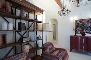 A room with a wooden bookshelf, a patterned armchair, a red cabinet, and a chandelier. - Trulli San Domenico by Perle di Puglia (Martina Franca)