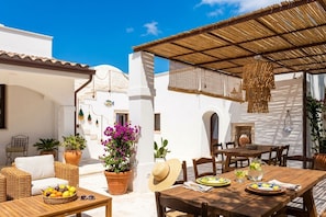 Eine Terrasse im Freien mit einem Holztisch, Korbmöbeln und Topfpflanzen.