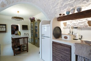 Eine rustikale Küche mit Steinwand, einem Holztisch und einem weißen Kühlschrank.