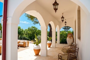 An outdoor covered patio with white arches, wicker furniture, potted plants, and hanging lanterns. - Trulli San Domenico by Perle di Puglia (Martina Franca)