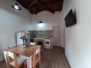 Una cucina compatta con tavolo e sedie, un rivestimento a mosaico e una TV a schermo piatto fissata al muro.