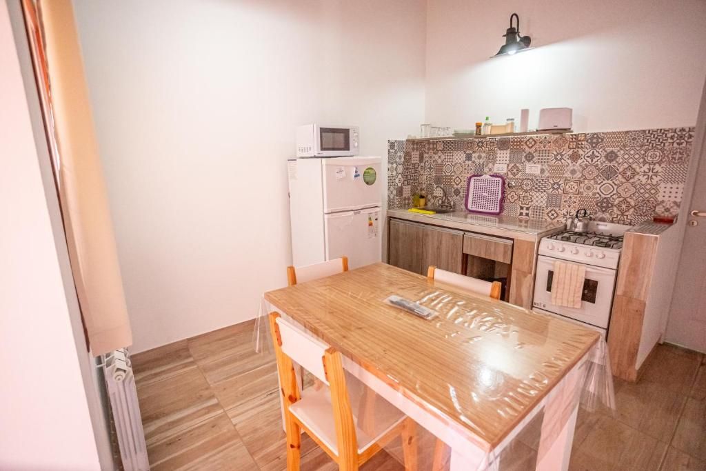 Eine kleine Küche mit Holztisch, weißen Schränken, einer Mikrowelle, einem Kühlschrank und einer gemusterten Spritzschutzwand.