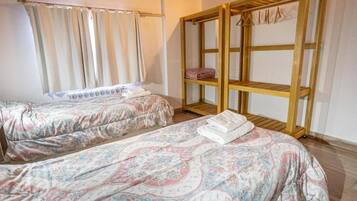 Una habitación con dos camas, un armario de madera y un ventanal con cortinas.