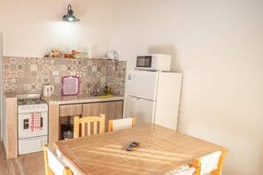 Une cuisine compacte équipée d’une cuisinière à gaz, d’un four à micro-ondes, d’un réfrigérateur et d’une table à manger avec des chaises.
