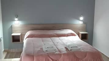 Un dormitorio con cama, cabecera de madera, mesitas de noche e iluminación en la pared.