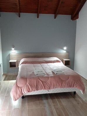 Un dormitori amb un llit, un panell de capçal de fusta, taules de nit i llums penjades a la paret.