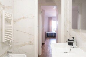 A hotel bathroom with a marble wall, a white sink, and a towel rack. - Marietta's House by BarbarHouse (Bari)