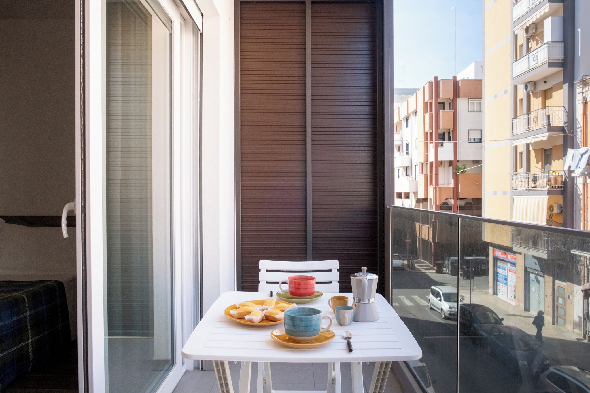 A balcony with a table set for breakfast, a chair, and a view of the street.