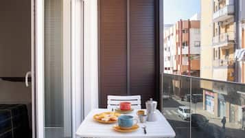 A balcony with a table set for breakfast, a chair, and a view of the street.