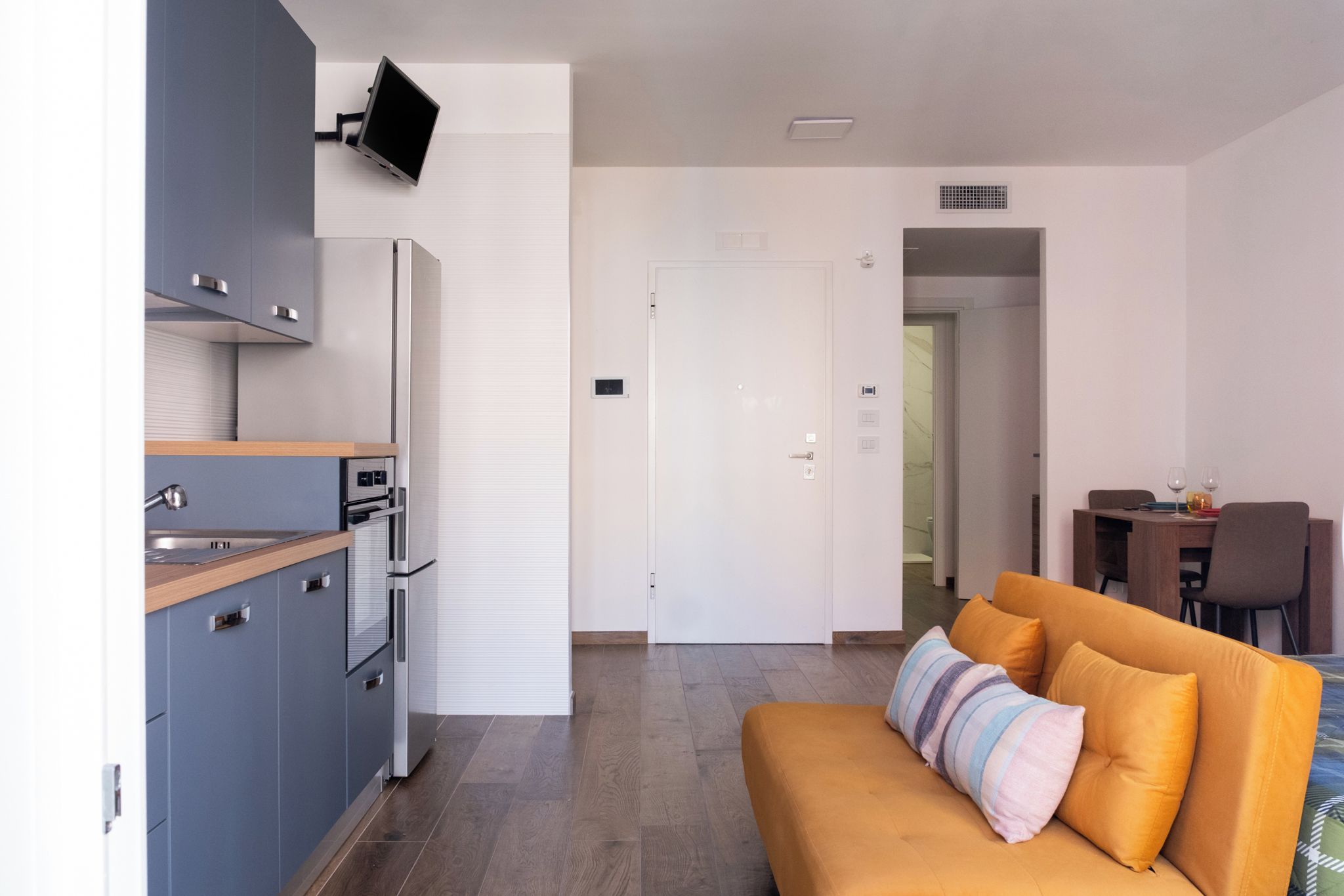 Una cocina moderna con electrodomésticos integrados, un comedor con mesa y sillas, y una sala de estar con sofá y cojines.