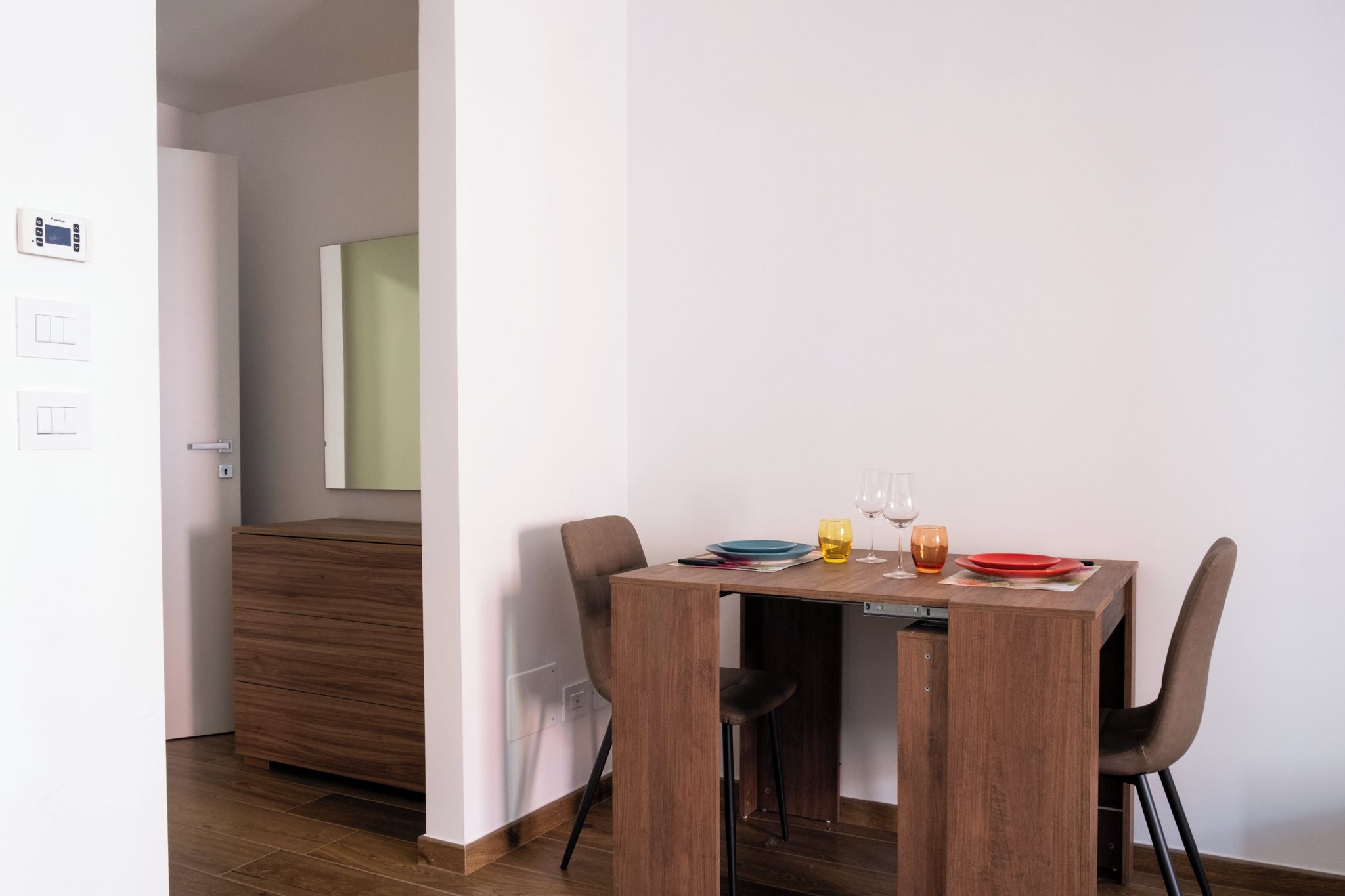 Un comedor moderno con una mesa de madera, dos sillas y un espejo en la pared.