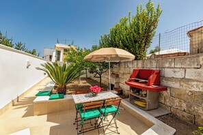Un patio con mesa, sillas, sombrilla, una parrilla y una pequeña zona ajardinada.