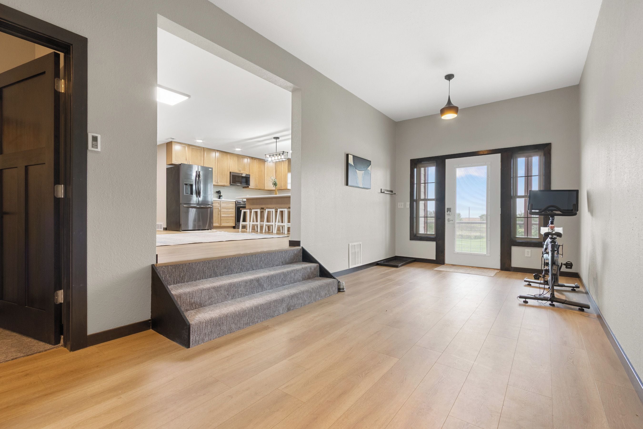 A spacious living area with hardwood flooring, a staircase leading to a kitchen, and a home gym.
