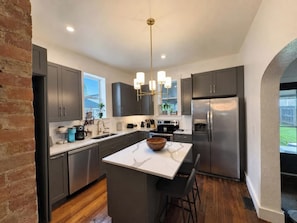 A modern kitchen with dark cabinets, a marble island, stainless steel appliances, and a hanging light fixture. - Fountain Square 3BR Sleeps 6 Near Downtown (Indianapolis)