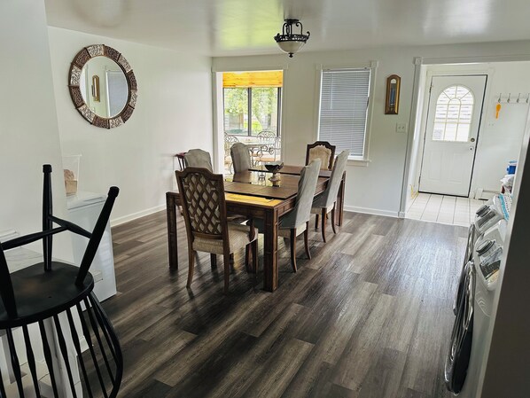 A dining area with a wooden table and chairs, a mirror on the wall, and a door with a window.