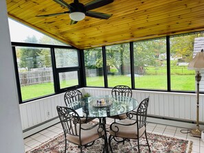 A sunroom with a glass table surrounded by chairs, a ceiling fan, and a view of a backyard.