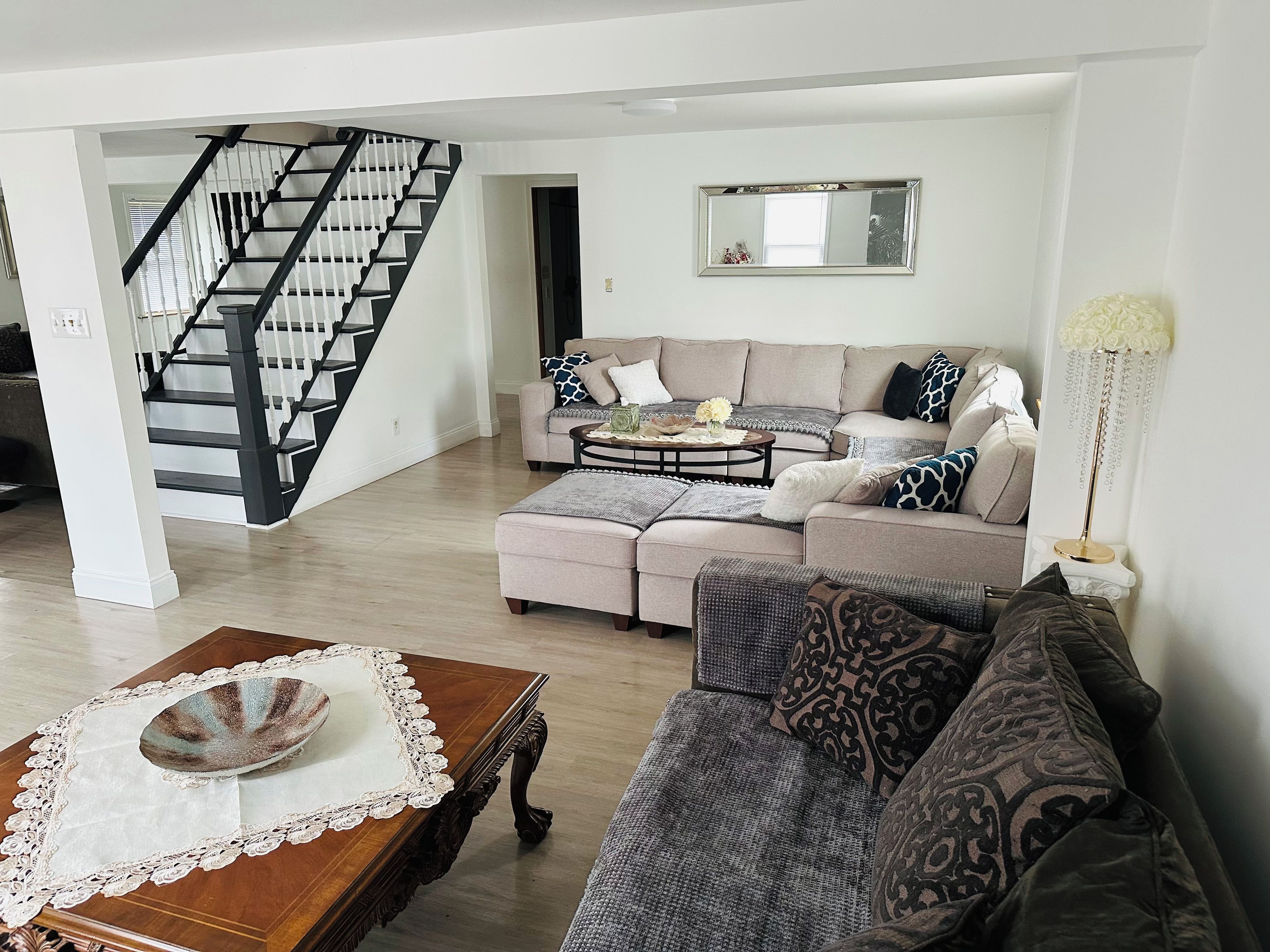 A living room with a staircase, a sofa set, a coffee table, and a decorative lamp.