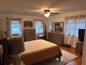 A bedroom with a bed, dresser, vanity, and a ceiling fan.