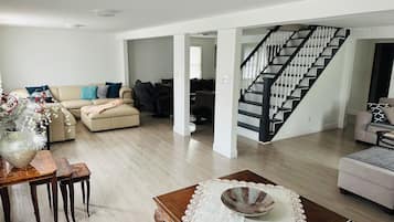 A spacious living area with a staircase, a dining table with chairs, and a sofa set.