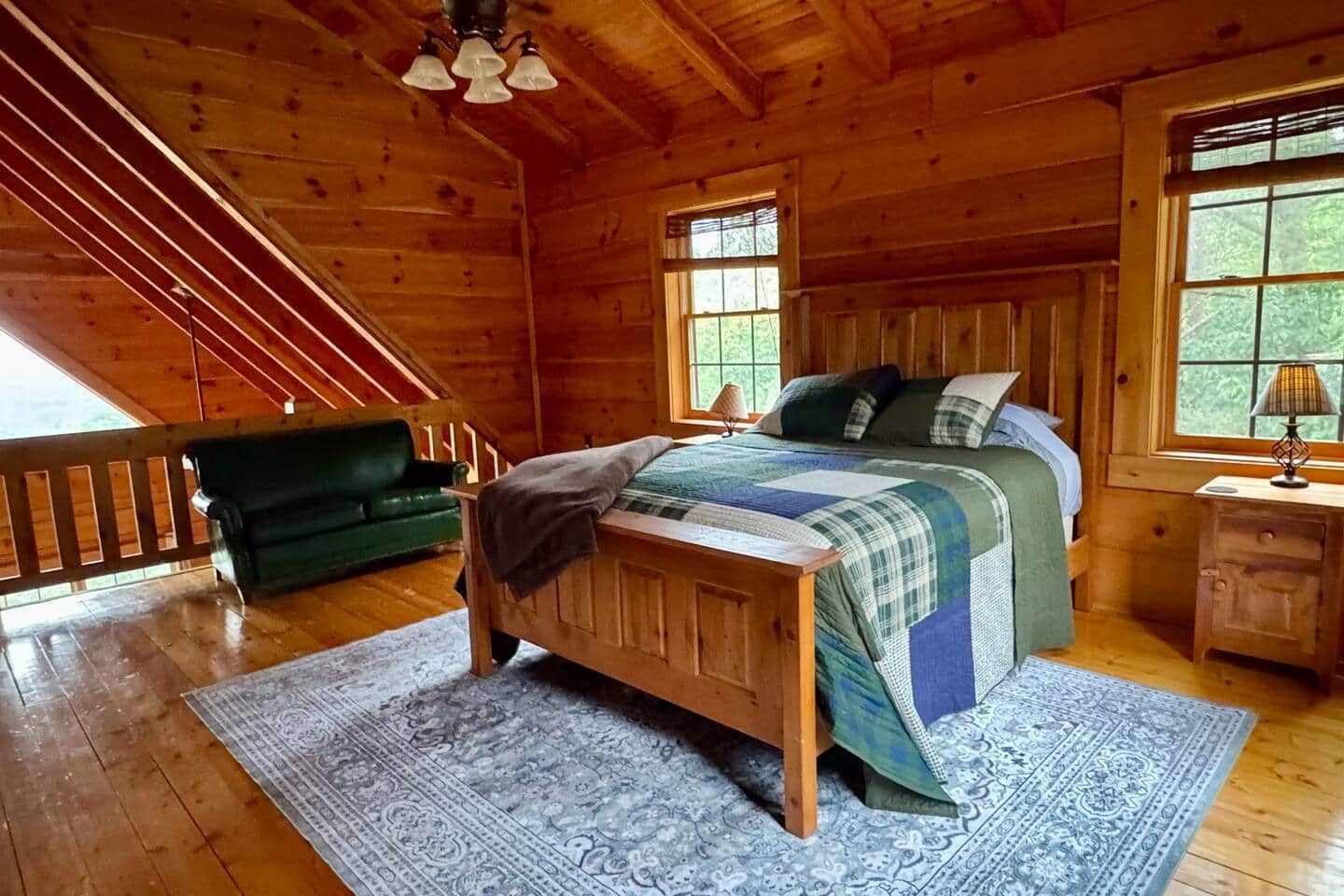 Een slaapkamer in een houten blokhut met een bed, een nachtkastje, een groene bank en een trap.