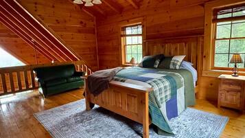 Een slaapkamer in een houten blokhut met een bed, een nachtkastje, een groene bank en een trap.