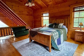 Een slaapkamer in een houten blokhut met een bed, een nachtkastje, een groene bank en een trap.