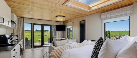 A modern bedroom with a large bed, a desk, and a view of the outdoors.