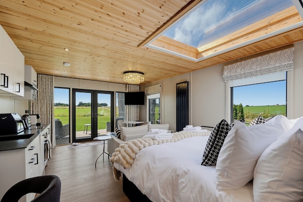 A modern bedroom with a large bed, a desk, and a view of the outdoors.