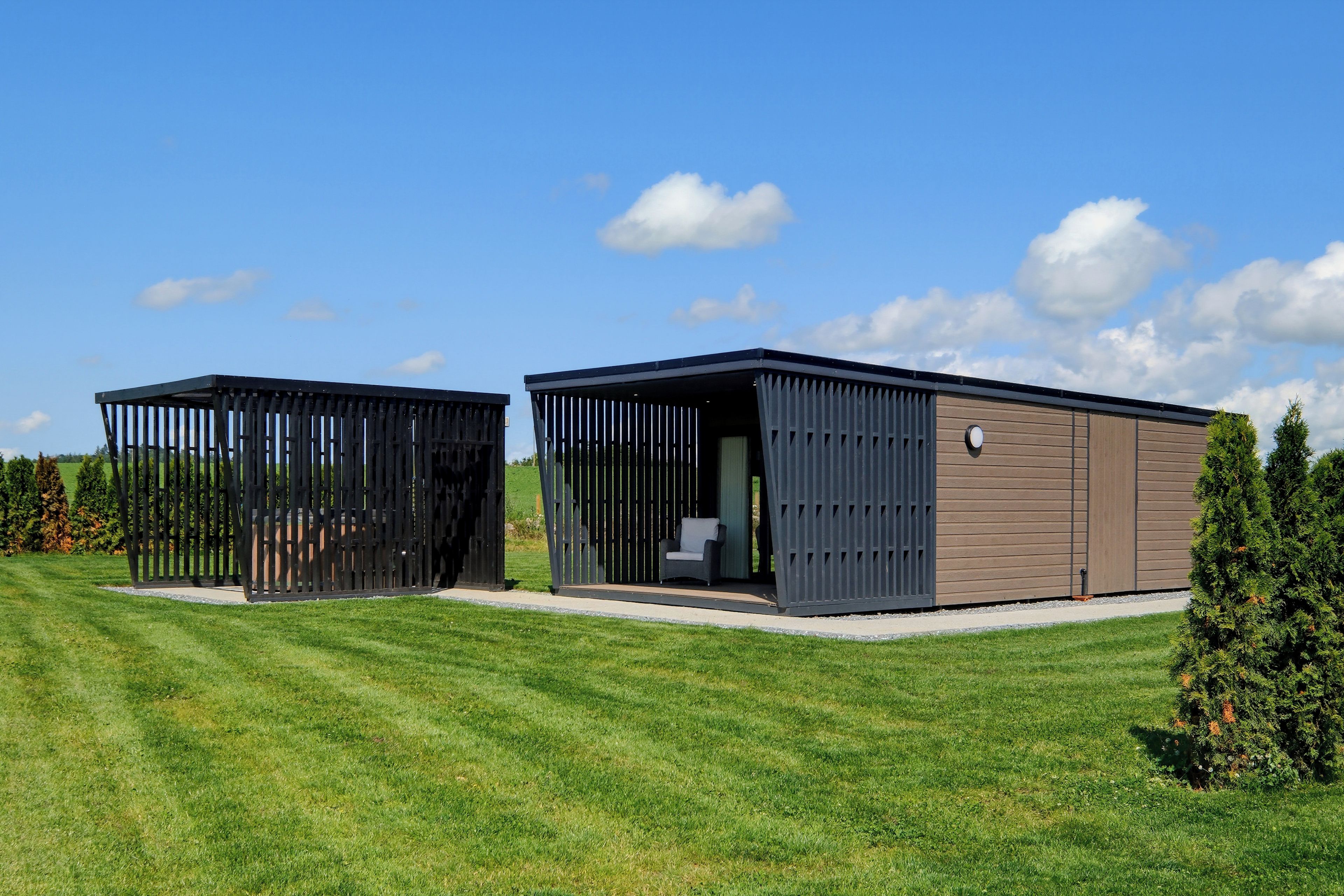 Two modern, detached buildings with open sides, set in a grassy field with a clear sky.