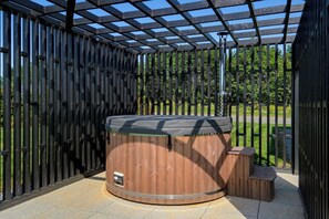 A hot tub under a pergola with a wooden fence and a grassy area in the background. - Luxury Lodge Milano with Hot Tub at Pitcaple Lodge Retreats, Aberdeenshire (Pitcaple)
