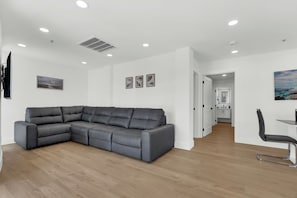 Een moderne woonkamer met een hoekbank, een flatscreen televisie en een eethoek met tafel en stoelen.
