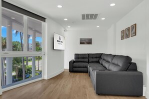 A modern hotel room with a large window, a sectional sofa, and a framed sign on the wall.
