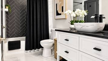 A modern bathroom with a white vanity, black towel, marble tiles, a black shower curtain, and a white toilet.