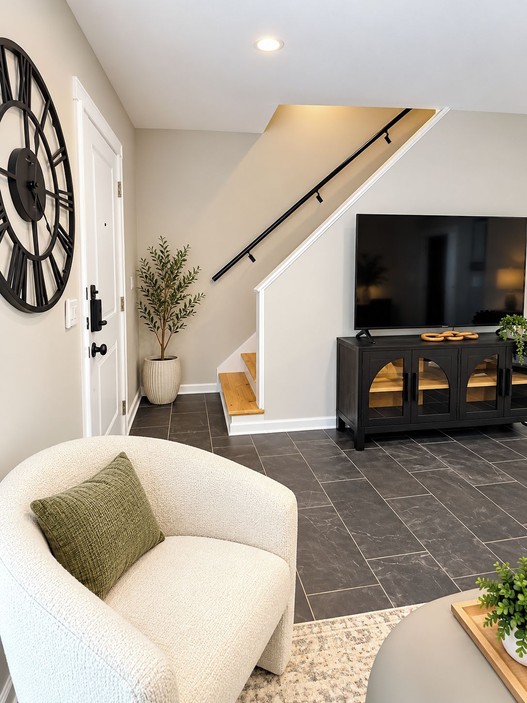 Un salon moderne avec un canapé, une grande horloge murale, un téléviseur à écran plat et un escalier menant à un niveau supérieur.