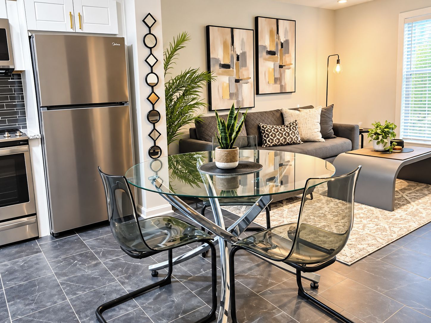 A modern kitchen with a stainless steel refrigerator, a glass dining table with chairs, and a living area with a sofa and decorative wall art.