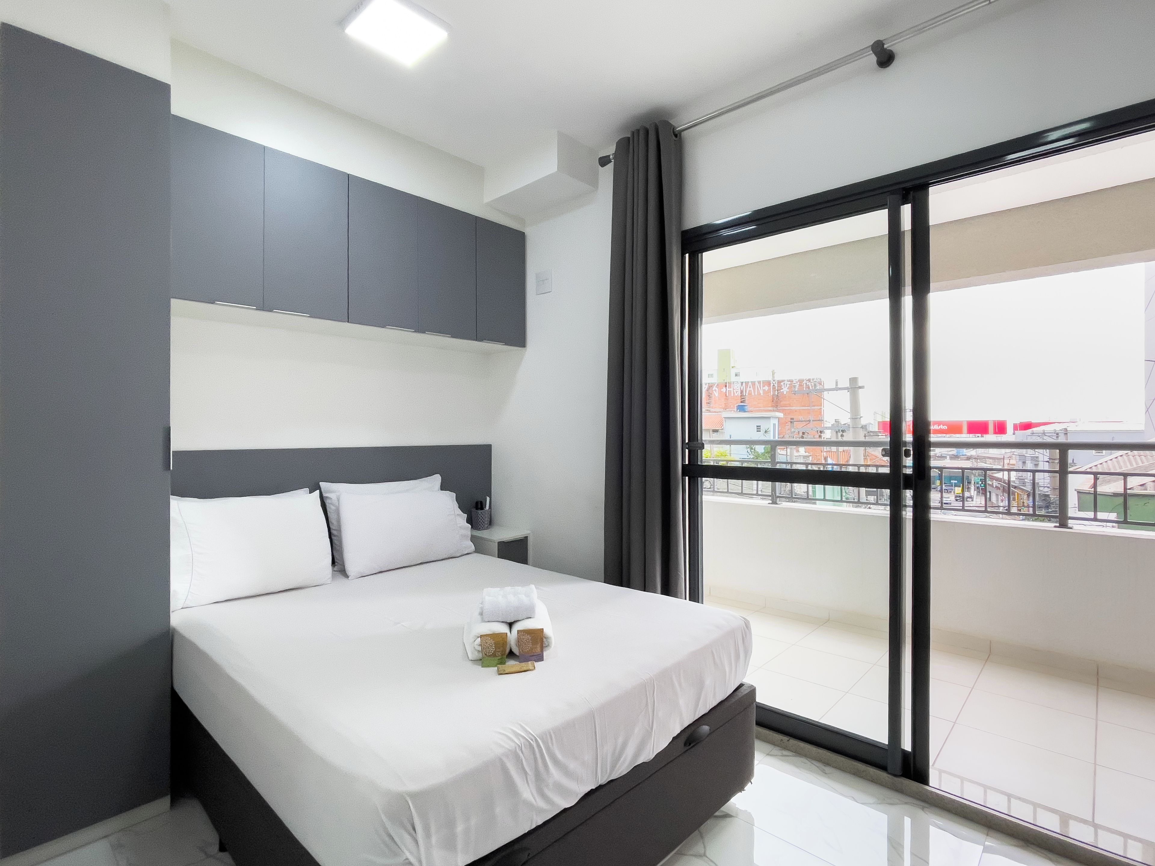 Een moderne hotelkamer met een groot bed, een nachtkastje en uitzicht op de stad door een groot raam.